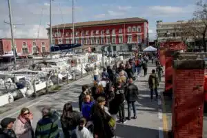 Porto turistico affollato con persone e barche a vela.
